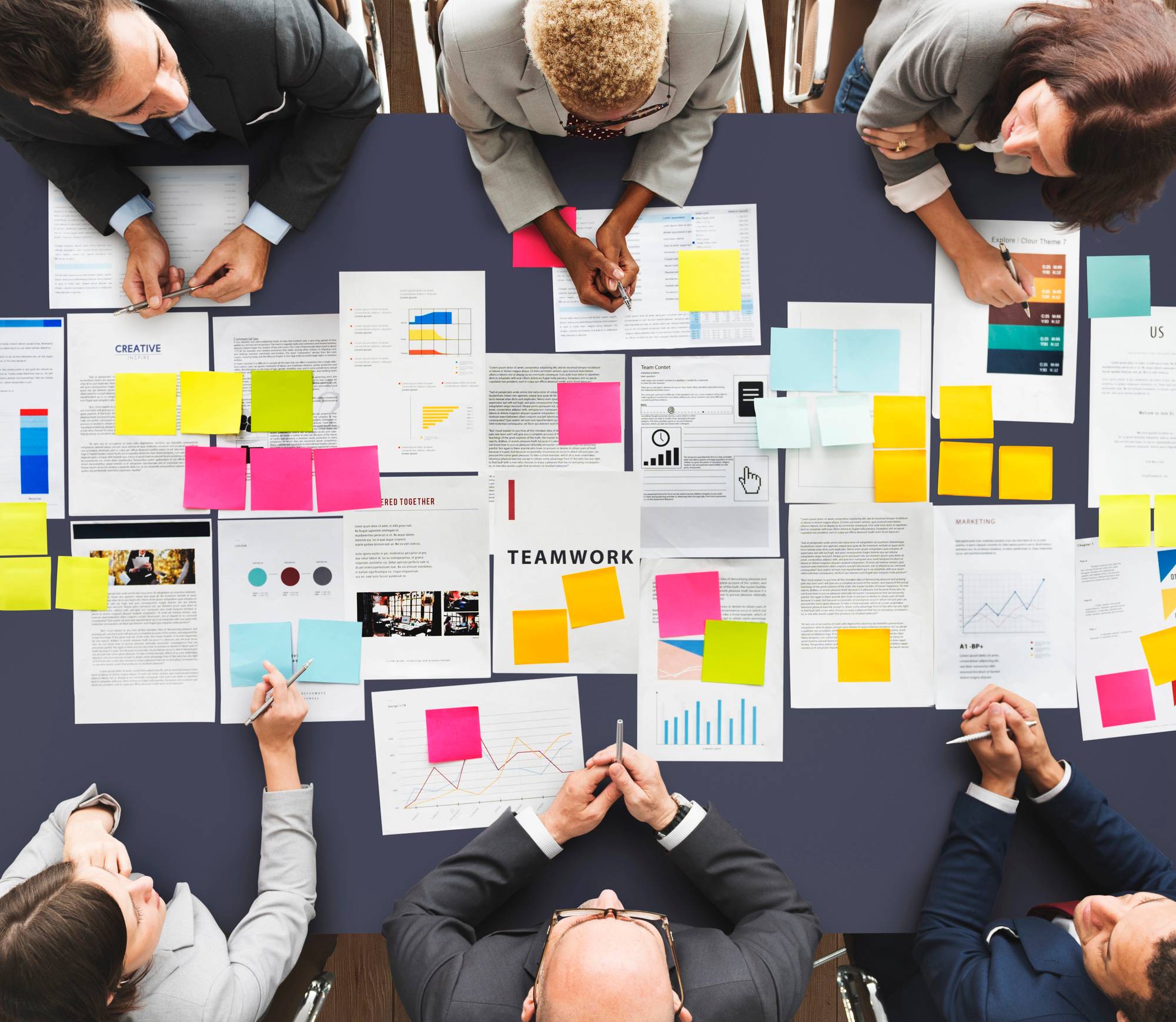 People working together at a table covered with papers, graphs, and colorful sticky notes.