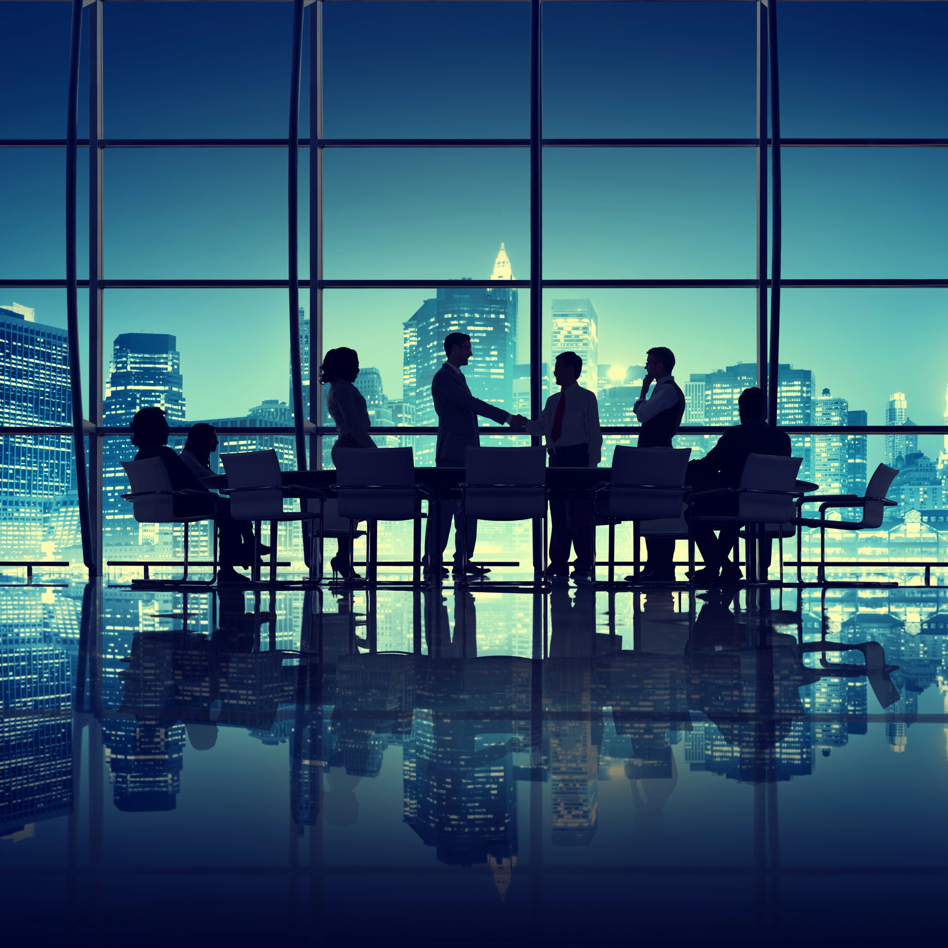 Agreement in the Office Silhouettes of business people in a conference room with large windows overlooking a city skyline at dusk.
